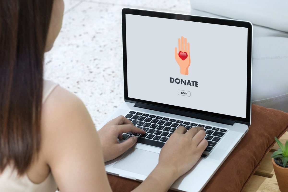 Woman on laptop with screen that shows Donate headline, Give button, and hand with heart