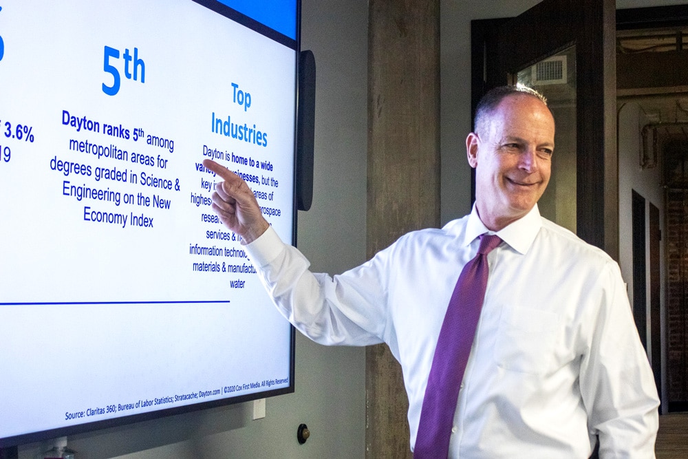 Man pointing at TV with "Dayton ranks 5th among metropolitan areas for degrees graded in Science & Engineering on the New Economy Index" on it